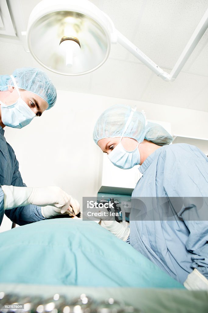 Surgeon Working A surgeon working in a small operating room with an assistant Adult Stock Photo