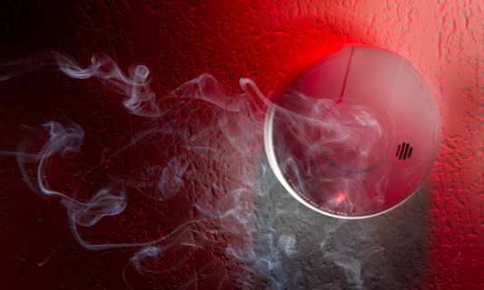 Smoke detector mounted on ceiling with white smoke, red warning light  and space for copy