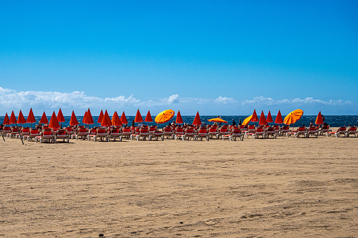 Gran Canaria, Spain - Feb 15, 2023: sandy beach with plastic chairs and umbrellas near Atlantic ocean in Maspalomas, Gran Canaria in Spain