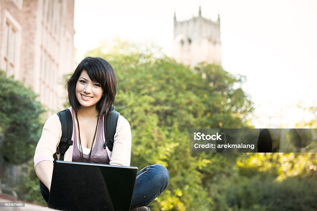 Young woman with laptop sits in front of a church Mixed race college student working on laptop at campus Happiness Stock Photo