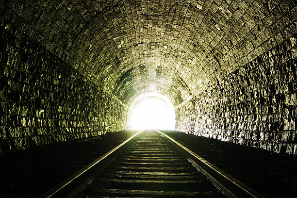 Light at the end of a brick tunnel with train tracks Light at the end of railroad tunnel. Natural lighting. tunnel stock pictures, royalty-free photos & images