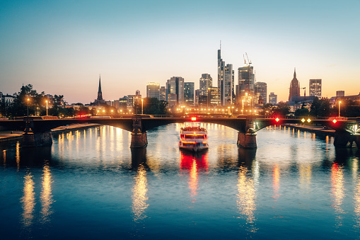 Frankfurt am Main skyline and Ignatz Bubis Bridge bridge during evening blue hour with mirror reflections in the river, Germany