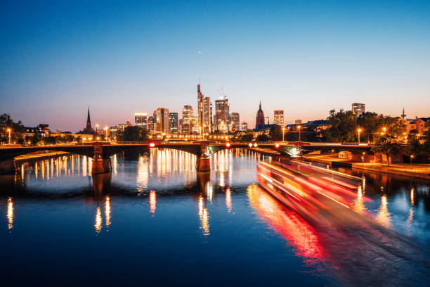 Frankfurt am Main skyline and Ignatz Bubis Bridge bridge during evening blue hour with mirror reflections in the river, Germany