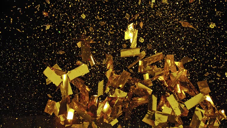 SLO MO LD Golden confetti bursting into the air against black background