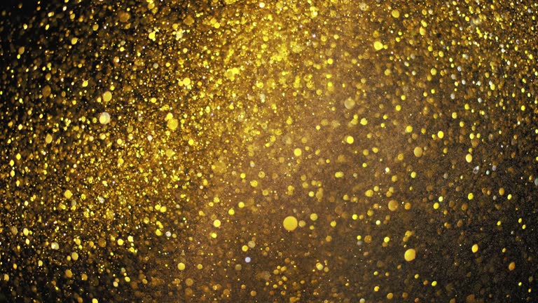 SLO MO LD Golden glitter bursting into the air against black background