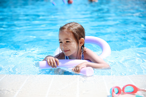 Child learning to swim in outdoor pool of tropical resort. Kids learn swimming. Exercise and training for young children. Little boy with colorful float board in sport club. Swimming baby or toddler.