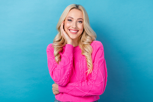 Photo of positive satisfied nice girl with wavy hairdo dressed pink sweater hold palm on cheekbone isolated on blue color background.