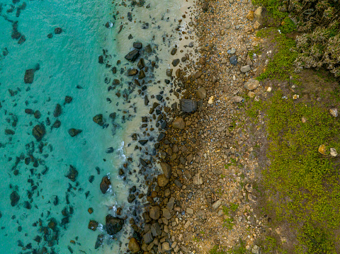 Abstract aerial photo of pebble beach next to blue sea with crashing waves, Con Dao, Con Son island, Ba Ria Vung Tau province