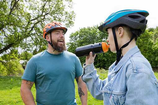 A shot of two people standing together before setting off on a community bike ride. They are in a field in Hexham, North East England. They are wearing casual clothing and cycling helmets, one of them drinking from a reusable water bottle.
