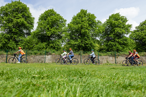 A side-view shot of a group of people cycling together on a community bicycle ride in Hexham, North East England. They are wearing casual clothing and cycle helmets, smiling and laughing as they cycle.