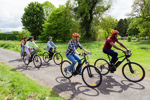 A shot of a small group of people cycling together on a community bicycle ride in Hexham, North East England. They are wearing casual clothing and cycle helmets, smiling and laughing as they cycle.