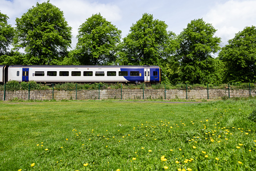 A side-view wide shot of a train moving through a rural setting in Hexham, North East England. It is a sunny day, there is a field in the foreground and trees behind.