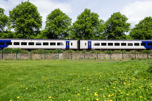 A side-view wide shot of a train moving through a rural setting in Hexham, North East England. It is a sunny day, there is a field in the foreground and trees behind.