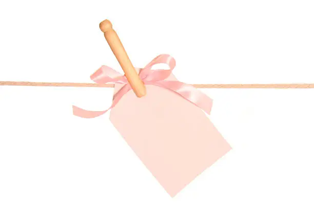 A gift tag with a pink bow on a clothesline held by an old-fashion clothes pin.