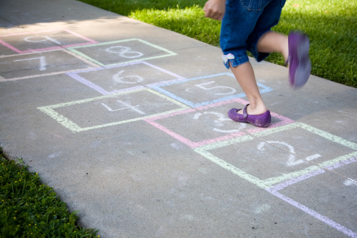 cropped image of little girl playing hopscotch on the sidewalk (shallow depth of field and some motion blur on her foot)