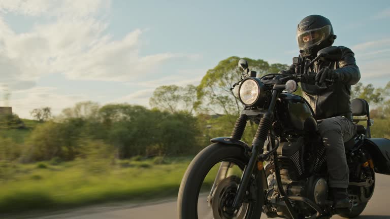 Low-angle tracking shot of a man driving a motorcycle through a country road.