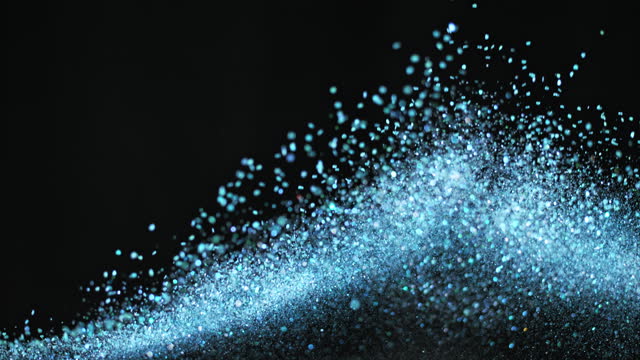 SLO MO LD Blue glitter bursting into the air against black background