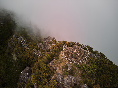 High angle view of young woman standing with her arms outstretched surrounded by fence on a mountain during foggy day. Copy space.