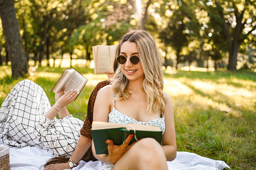 Blonde woman and her friends reading books on a picnic date in the park