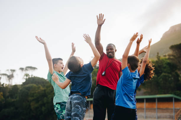 school coach and his team celebrating in a field - soccer child coach childhood imagens e fotografias de stock