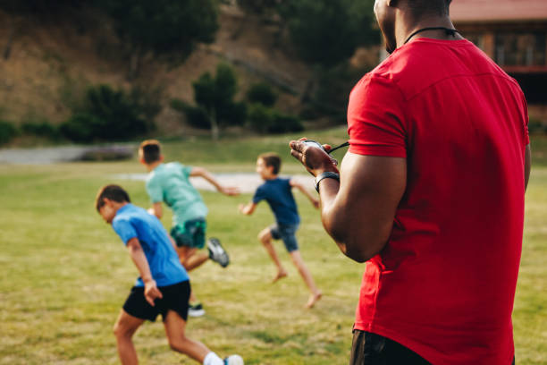 Sports trainer coaching a primary school team. PE teacher having a running session with a group of elementary school children. Sports and recreation in school.