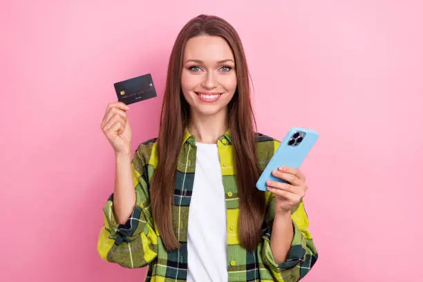 Photo of charming cheerful person toothy smile hold showing plastic debit card smart phone isolated on pink color background.