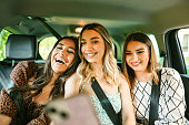 Three beautiful girls taking selfies while riding in the back seat of the car