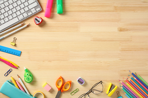 Back to school concept. Frame border of colorful school supplies on wooden desk table. Flat lay, top view.