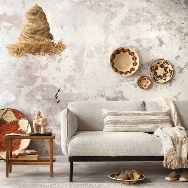 istock Interior design of ethnic composition living room interior with grey sofa, colorful wicker, boho straw lamp, gray concrete wall, bench and personal accessories. Home decor. Template. 1521997347