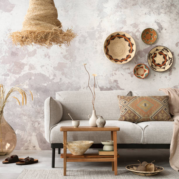 istock Interior design of ethnic composition living room interior with grey sofa, colorful wicker, boho straw lamp, gray concrete wall, bench and personal accessories. Home decor. Template. 1521997348