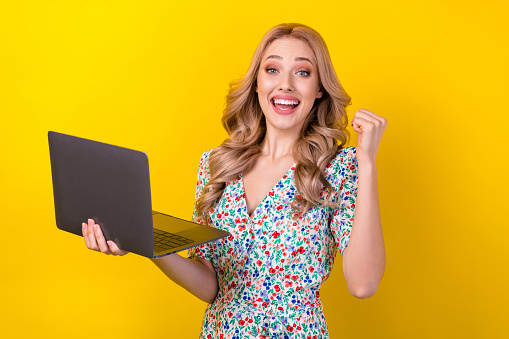 Retrato de alegre dama alegre usar ropa elegante sostener macbook levantar el puño regocijar descuento de venta aislado sobre fondo de color amarillo photo