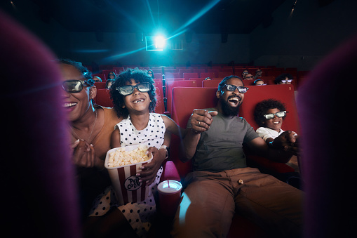 Cheerful black family having fun while watching a 3D movie in cinema.