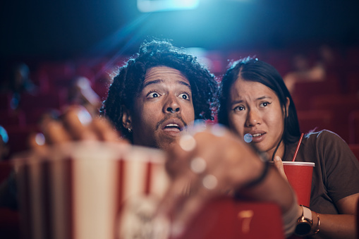 Fearful diverse couple watching a crime movie in cinema. Focus is on black man.