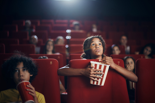 African American girl eating popcorn while watching a movie projection in cinema.