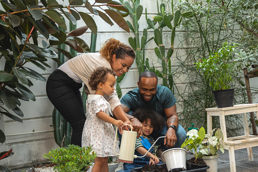 Happy African family as they enjoy a fun and fulfilling day in their outdoor garden. The parents, along with their children, come together to plant beautiful flowers and greenery in pots. Handheld