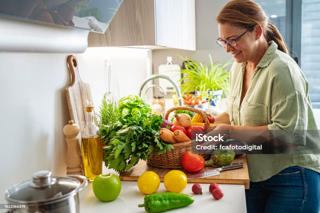 Woman with basket full of fresh vegetables in kitchen Healthy Eating Stock Photo