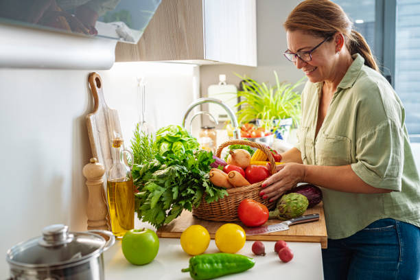 Woman with basket full of fresh vegetables in kitchen stock photo