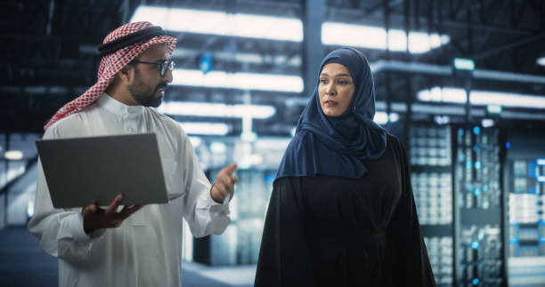 Middle Eastern Computer Engineer and Cybersecurity Specialist Work in Server Facility. Muslim Female and Male Managers Talk, Perform System Maintenance Check with Laptop Computer ingeniero informático de oriente medio y especialista en ciberseguridad trabajan en instalaciones de servidores. gerentes musulmanes y gerentes femeninos hablan y realizan una verificación de mantenimiento del sistema con una computadora portátil