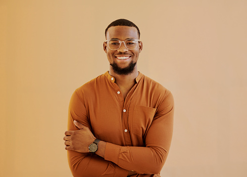 A young businessman standing wearing eyeglass while smiling into the camera with his arms folded with copy space. Stock photo
