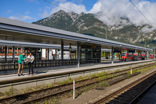 A wide angle view of a same sex couple who are travelling in Germany in Garmisch. They have arrived at the station and are looking at a map trying to work out and plan their day. They are carrying rucksacks and looking at a full size map.