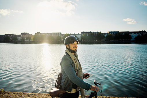 Young man strolling beside a lake in the city of Copenhagen, listening to an audiobook or a podcast.