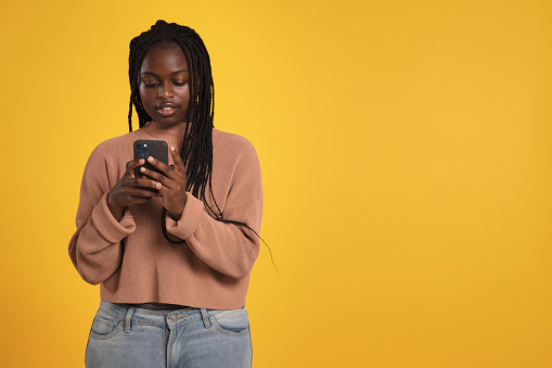 Portrait of a cool young adult woman/teenager holding her smartphone against a yellow background