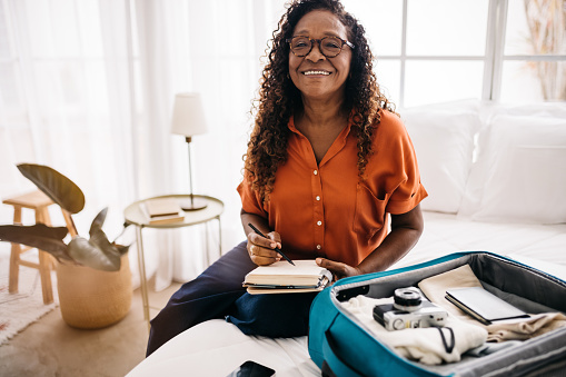 Happy senior traveler using a packing checklist as she plans an international trip. Retired woman packing her vacation essentials, preparing to embark on an exciting and unforgettable adventure trip.