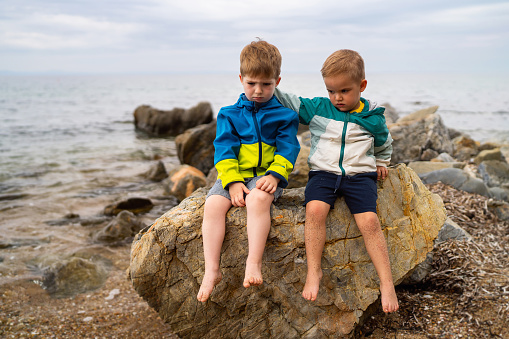 Two little brothers sitting on the rocky beach.