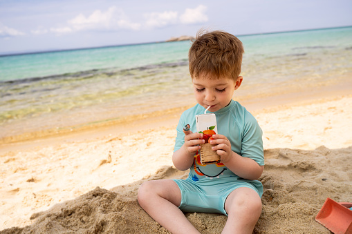 Little boy drinking juice on the beach.