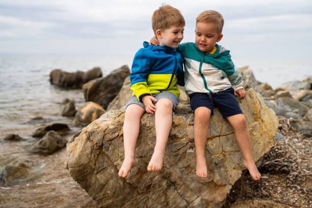 Two little brothers sitting on the rocky beach.