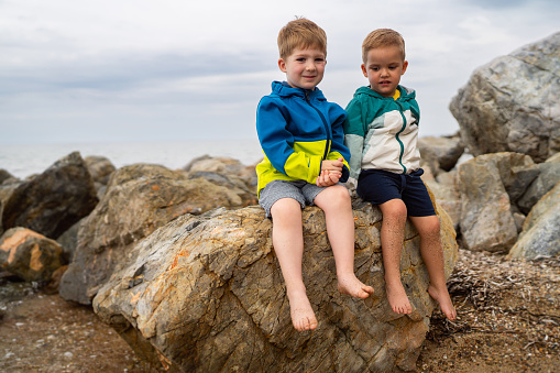 Two little brothers sitting on the rocky beach.