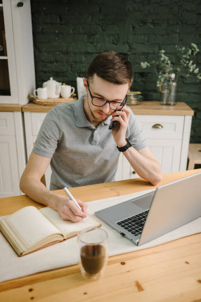 istock Writing in notebook. Serious man working, learning online on laptop in home office. Trading cryptocurrency. Trader talk on phone, investor broker analyzing indexes. Freelance. Marketing. Communication 1522189844