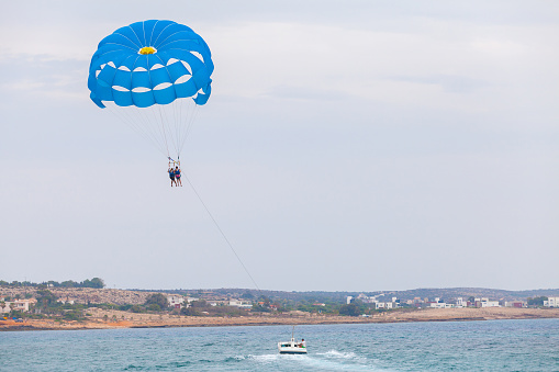 Ayia Napa, Cyprus - June 16, 2018: Parasailing in Agia Napa bay, motor boat and blue parachute with tourists