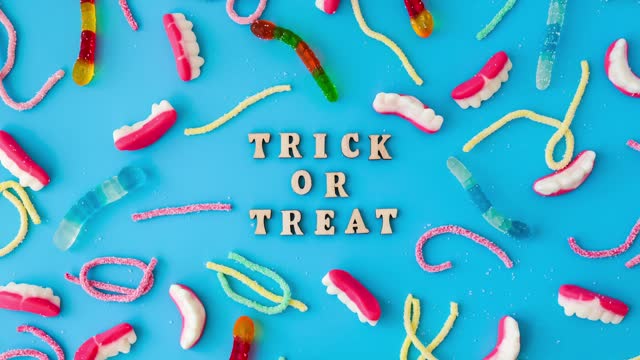 4k zoom in out Halloween concept. Halloween party decorations with words TRICK OR TREAT, sweets, top view flat lay on blue background